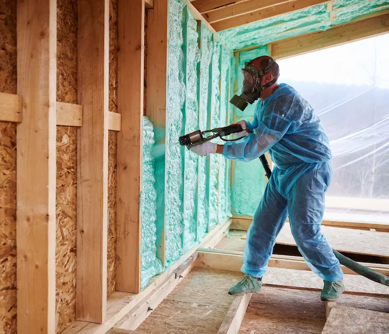 Worker spraying foam insulation inside a cottage